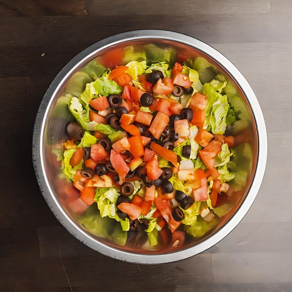 A metal bowl filled with fresh green lettuce, diced red tomatoes, and sliced black olives.