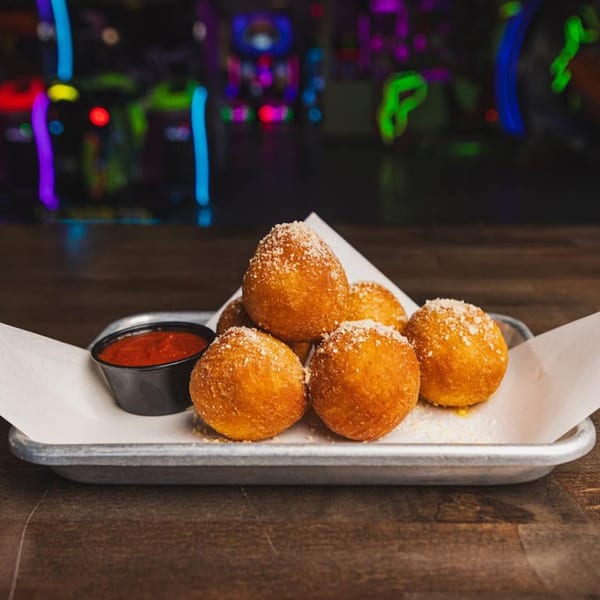 Golden-brown fried cheese balls, sprinkled with parmesan, and a side of marinara sauce on a metal tray.