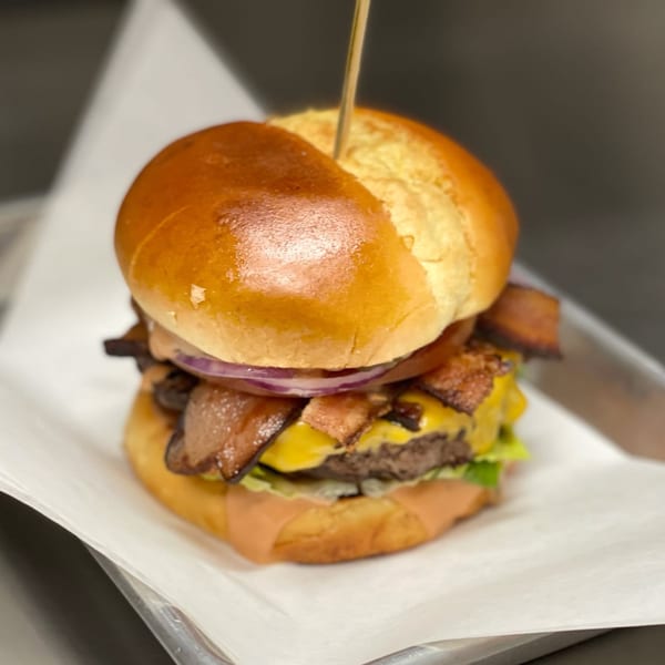 A bacon cheeseburger with red onion and lettuce on a brioche bun, served on white paper.