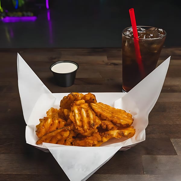 Crispy waffle fries in a paper-lined basket with a side of ranch and a drink.