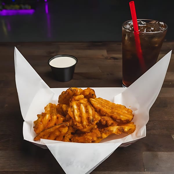 A basket of IWingz waffle fries with a side of ranch and a soda on a wooden table.