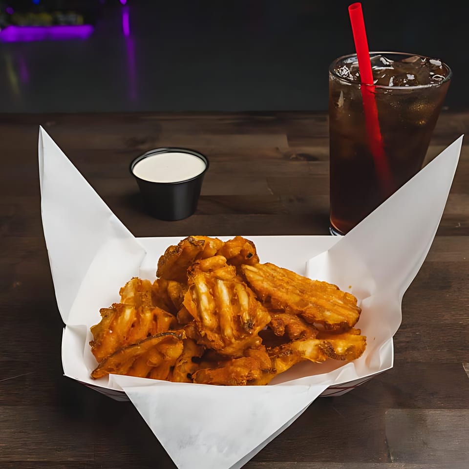 A basket of IWingz waffle fries with a side of ranch and a soda on a wooden table.
