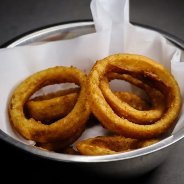 Golden-brown onion rings in a metal bowl lined with white paper from IWingz.