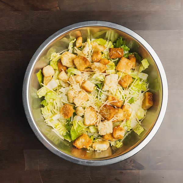 A Caesar salad with crisp lettuce, croutons, and shredded cheese in a metal bowl.