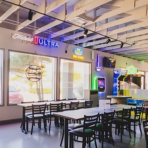 Interior of IWingz restaurant with tables, chairs, neon signs, and arcade games.