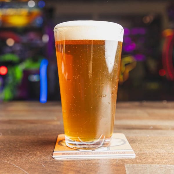 A tall glass of IWingz beer with a foamy head sits on a coaster on a wooden table.
