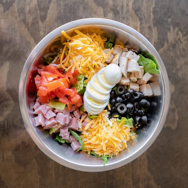 Overhead view of a large salad with ham, chicken, tomatoes, olives, cheese, and sliced egg.